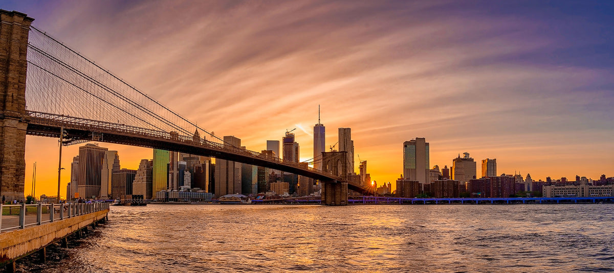 Brooklyn Bridge and Lower Manhattan skyline silhouette against a vibrant sunset sky over the East River
